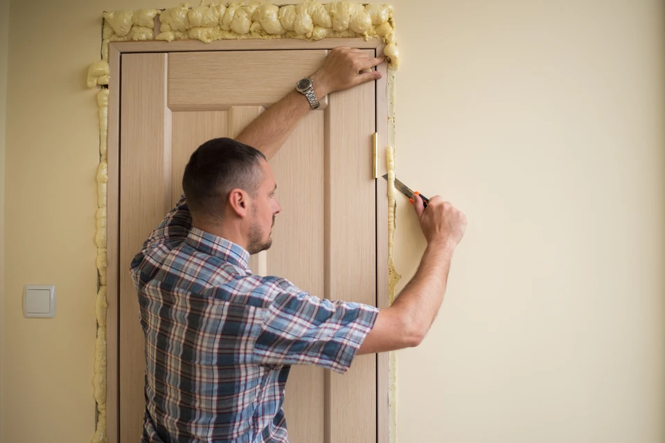 Un homme en chemise à carreaux installe une porte d'intérieur en bois dans un cadre de porte