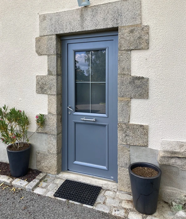Entrée résidentielle extérieure avec porte d'entrée contemporaine gris-bleu, encadrement en pierre de taille naturelle, mur crépi beige