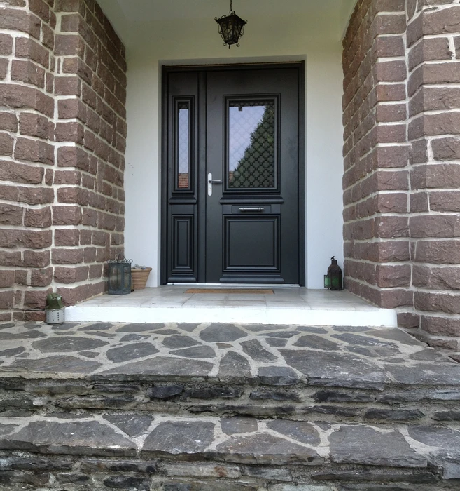 Entrée résidentielle avec porte d'entrée noire à panneaux et vitrage décoratif, encadrée par des murs en briques apparentes