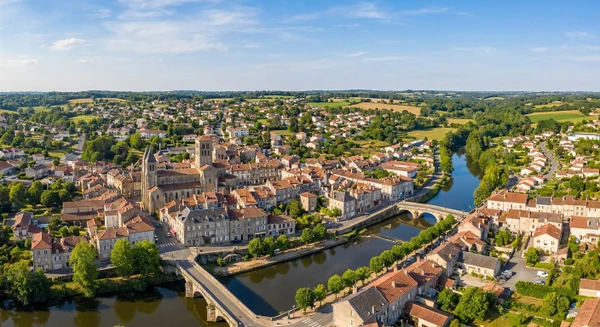 Photographie panoramique ou vue aérienne de la ville de Saint-Junien montrant ses caractéristiques urbaines et architecturales distinctives (centre-ville, églises, quartiers résidentiels, paysage local de Haute-Vienne), avec une esthétique professionnelle et moderne, sans texte ni logo.