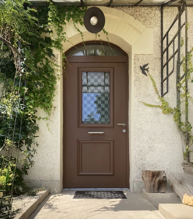 Entrée résidentielle extérieure avec porte en bois marron à panneau vitré décoratif et imposte cintrée