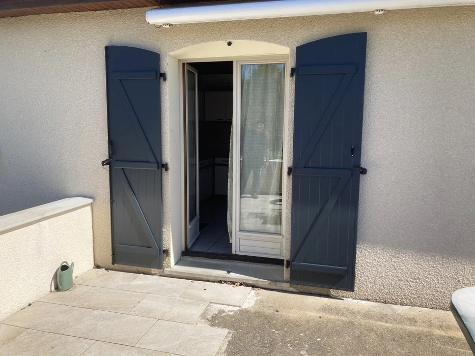 Extérieur d'une habitation avec porte-fenêtre à deux vantaux ouverte donnant sur une terrasse carrelée
