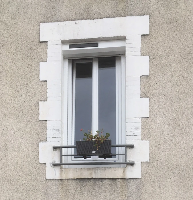 Façade extérieure d'immeuble avec fenêtre à la française à double battant blanc, encadrée par des pierres de taille blanches sculptées en saillie